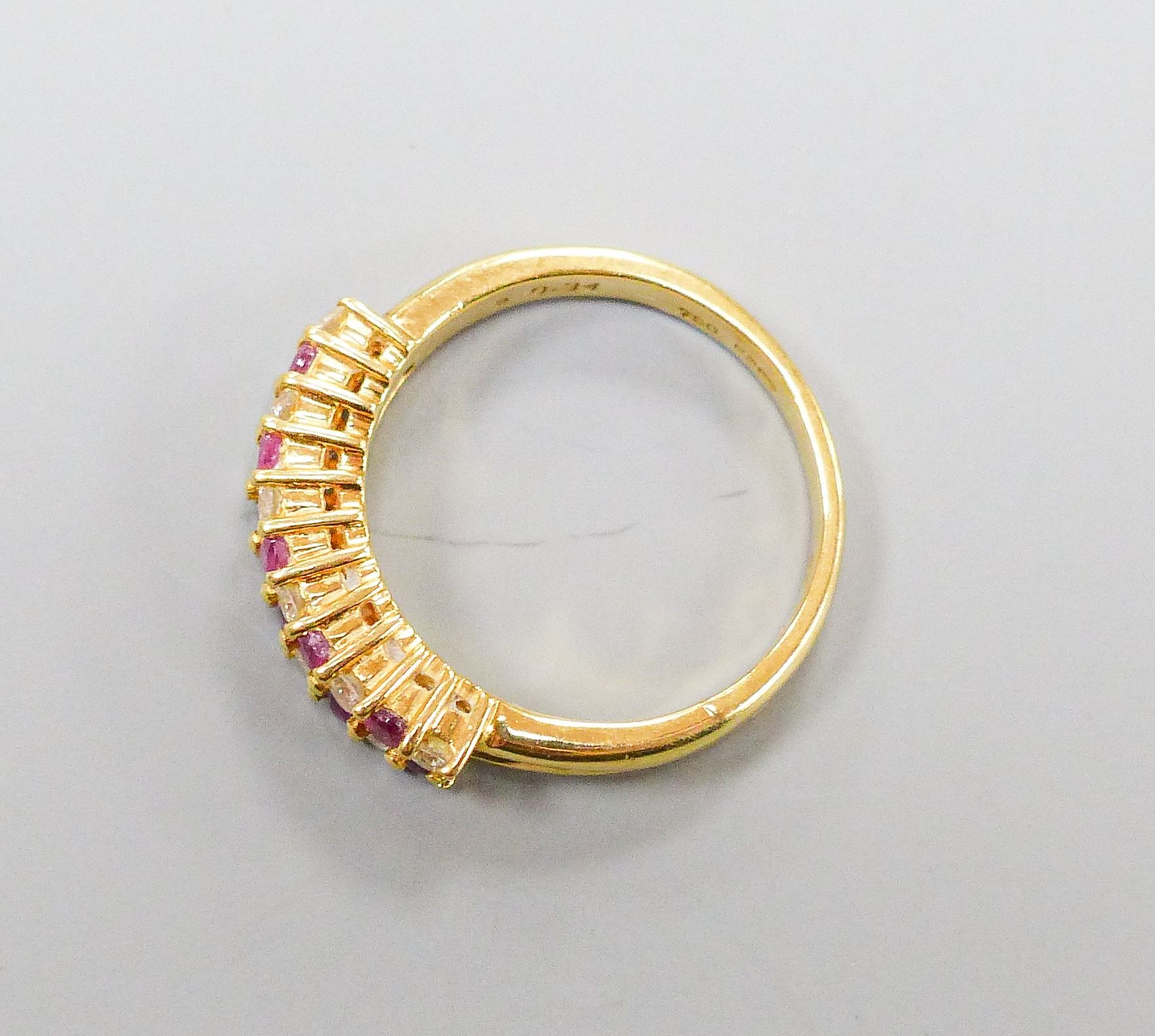 A modern 18ct gold, ruby and diamond set two row half hoop ring, size O, gross 5.3 grams.